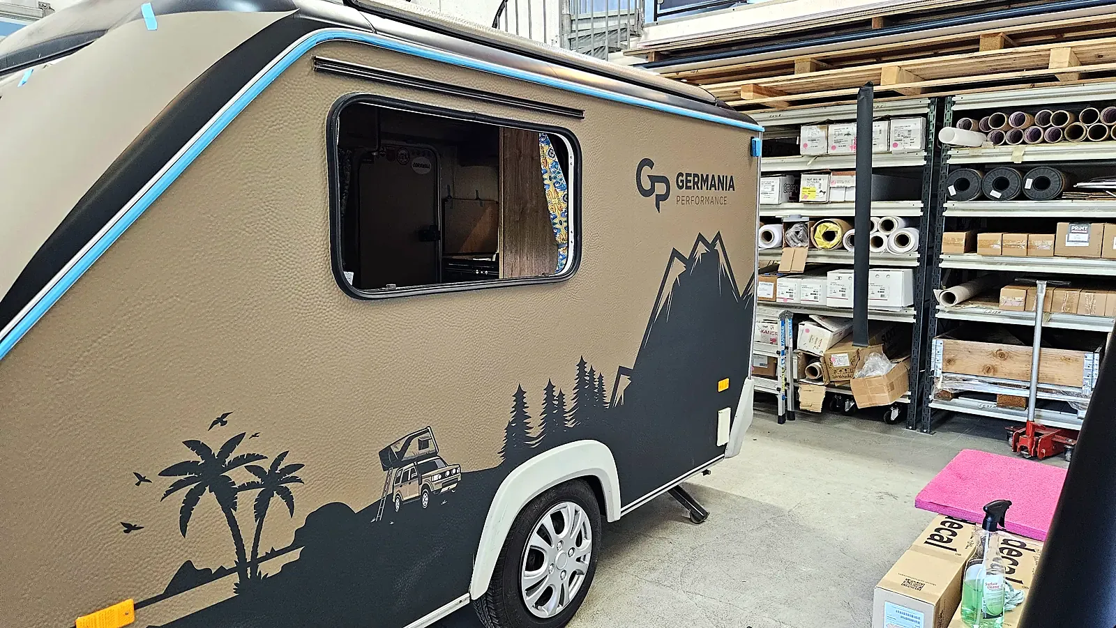 Siden på campingvogna med printet motiv av fjell, skog, palmer og en Land Rover med taktelt