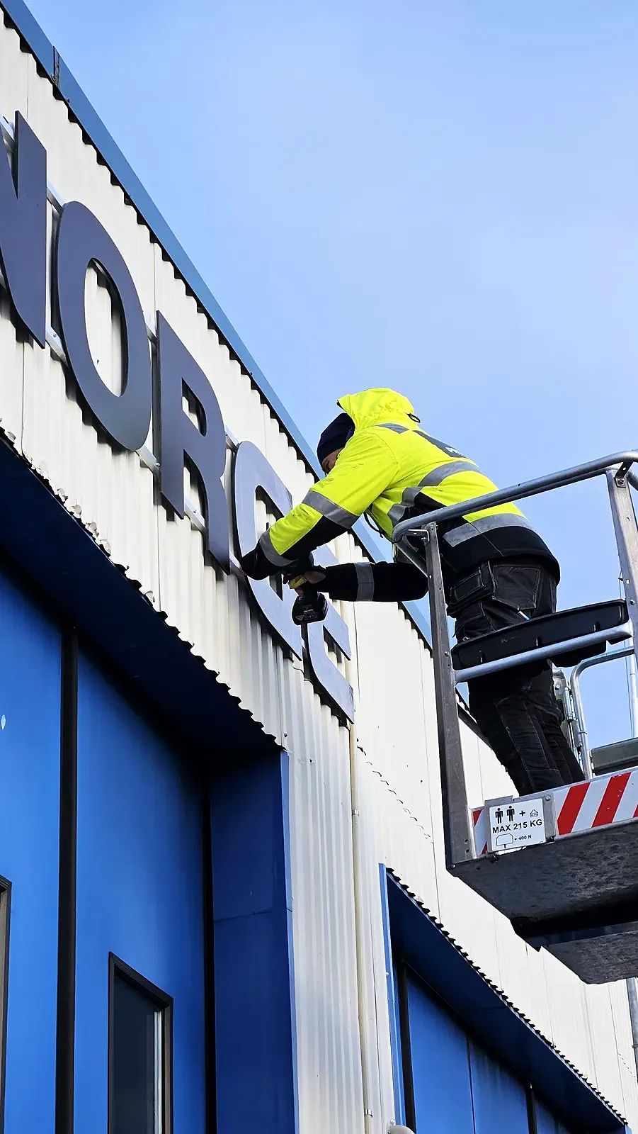 Montør i lift monterer bokstaver på fronten av bygget